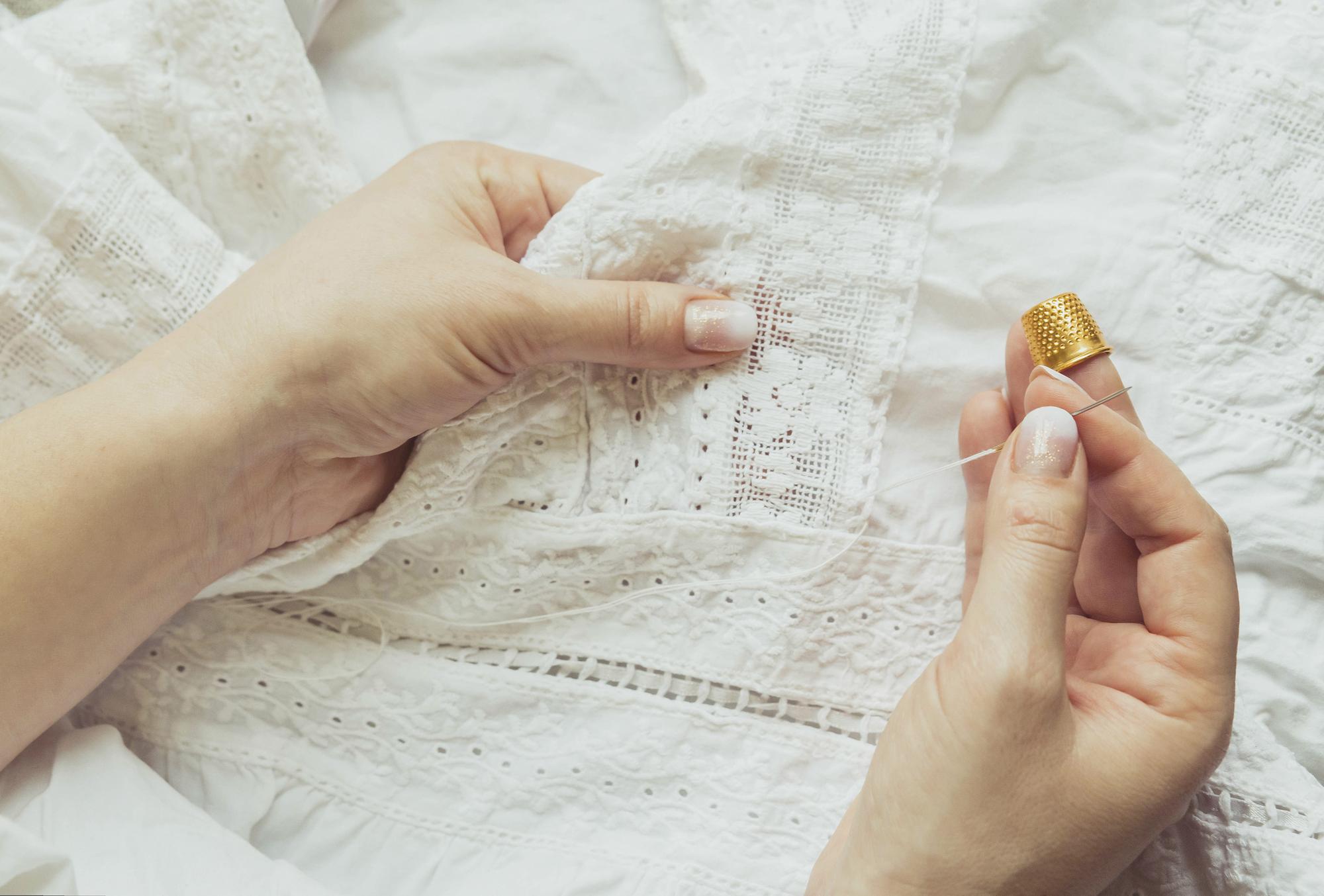 Close-up of artisan hand embroidering linen with gold thread